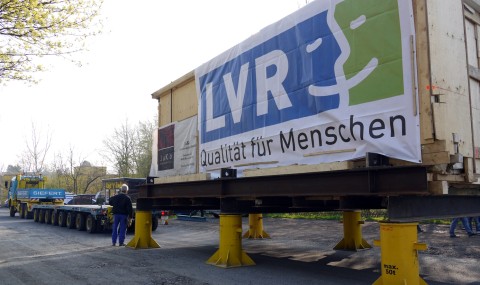 Auf einem Parkplatz werden die Container vom Transportwagen auf einen kleineren Lastwagen umgeladen. Foto: LVR-Freilichtmuseum Kommern, Andrea Nowotny